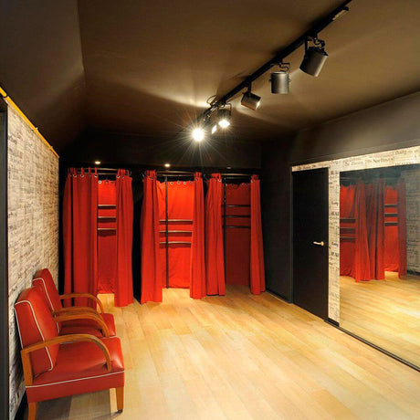Room with red curtain changing stalls, wooden floor, and spotlight lighting, ideal for fashion showcases.