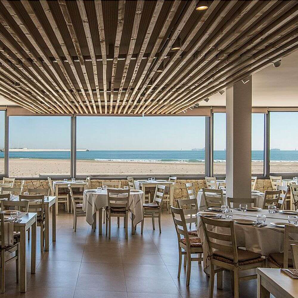 Moderne Restaurant mit Meerblick, hellen Holztischen und eleganter Inneneinrichtung nahe dem Strand.