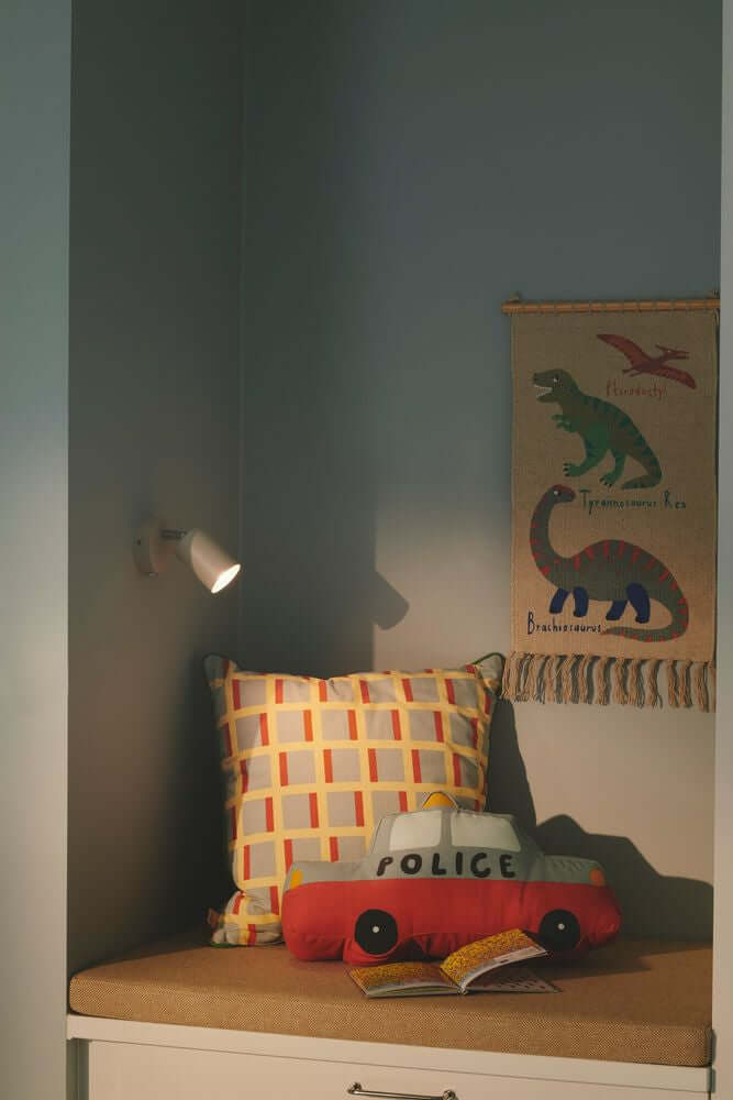 Explore Wandleuchte beleuchtet gemütliche Ecke mit Kissen und Spielzeugauto im Kinderzimmer.