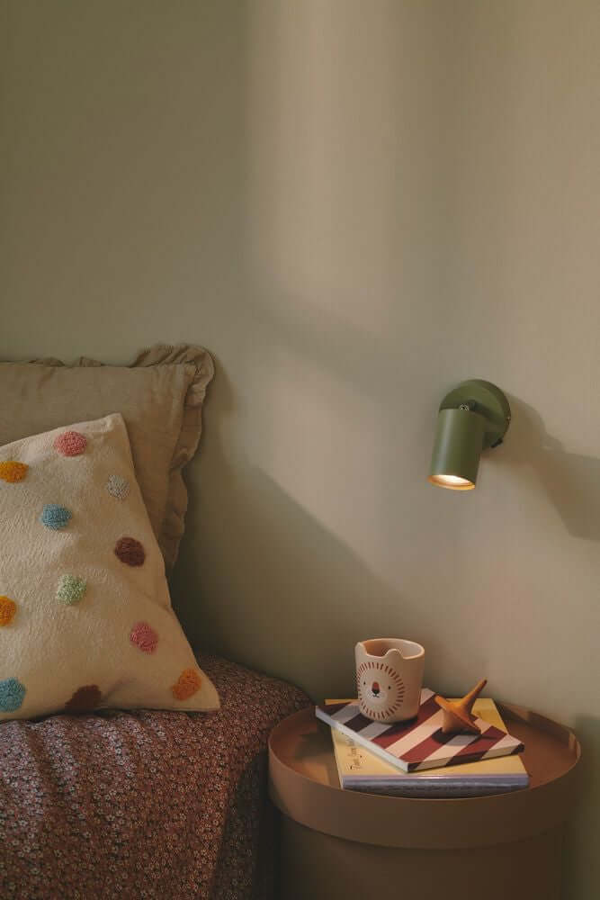 Explore Wandleuchte an einer Wand neben einem Bett mit Kissen und Büchern auf einem Tisch.