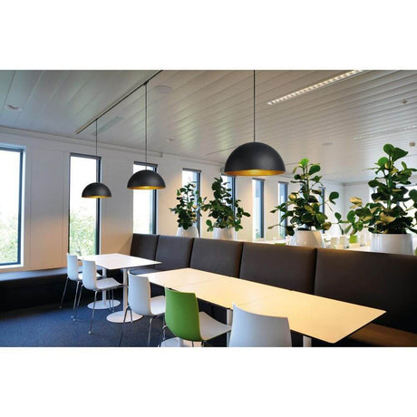 Moderne Forchini M Pendelleuchten in schwarz und gold über einer hellen Esstischgruppe mit Pflanzen.