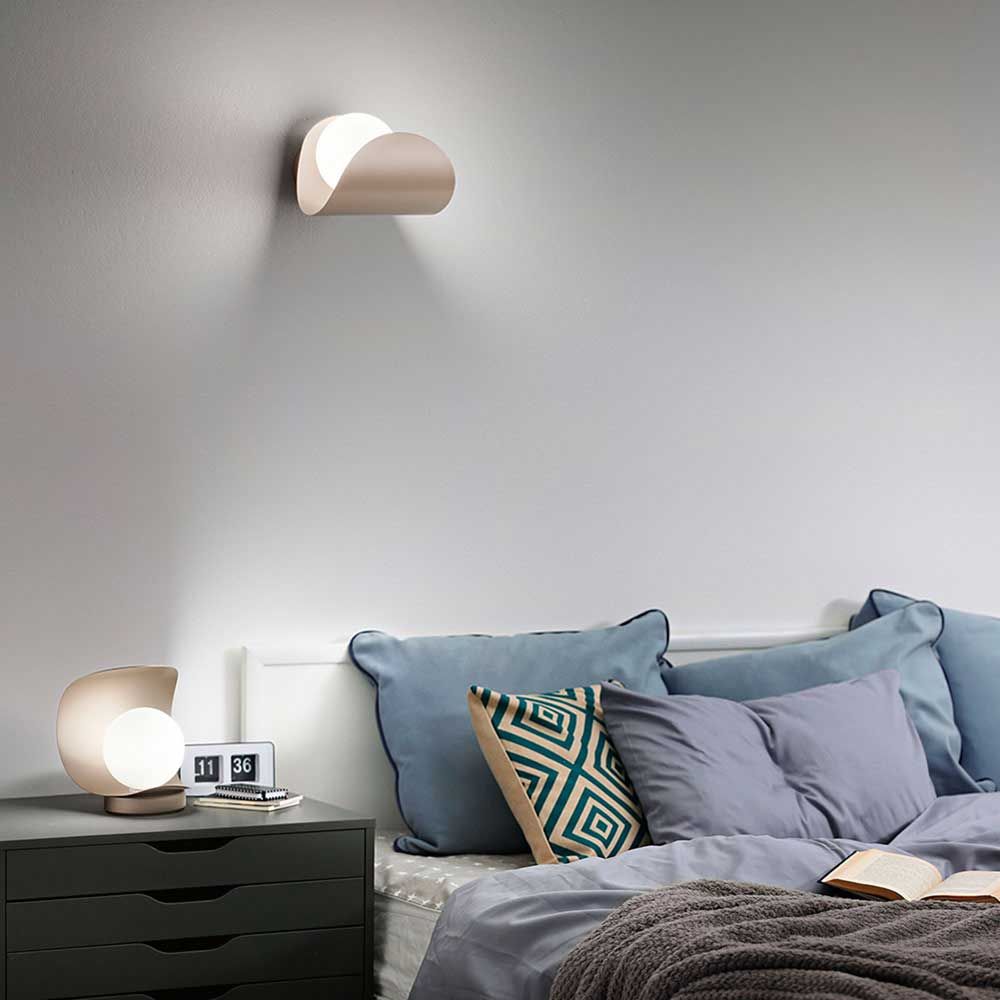 Adria LED Wandleuchte aus Metall über einem Bett mit Kissen und Tischlampe, modernes Design für stilvolle Innenräume.