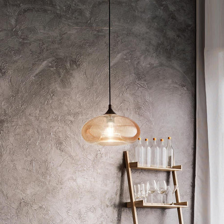Ela glass pendant light in amber above a wooden table with glass bottles and glasses in the background.