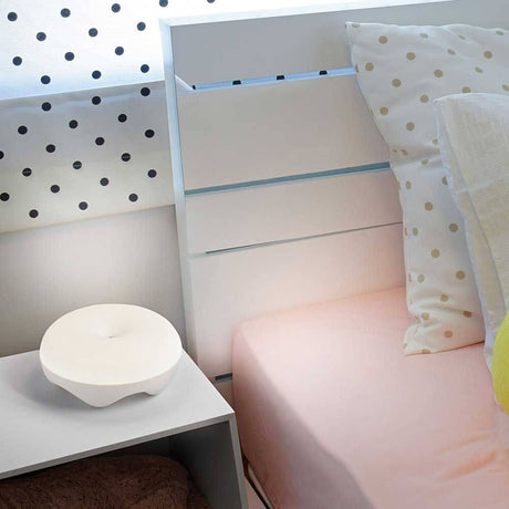LED Rechargeable table lamp Bluma on a bedside table in the bedroom, surrounded by pillows and a patterned curtain.