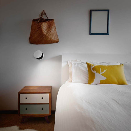 LED Wandlampe Ara 720+360lm Weiß an der Wand über einem Bett mit Kissen und Nachttisch