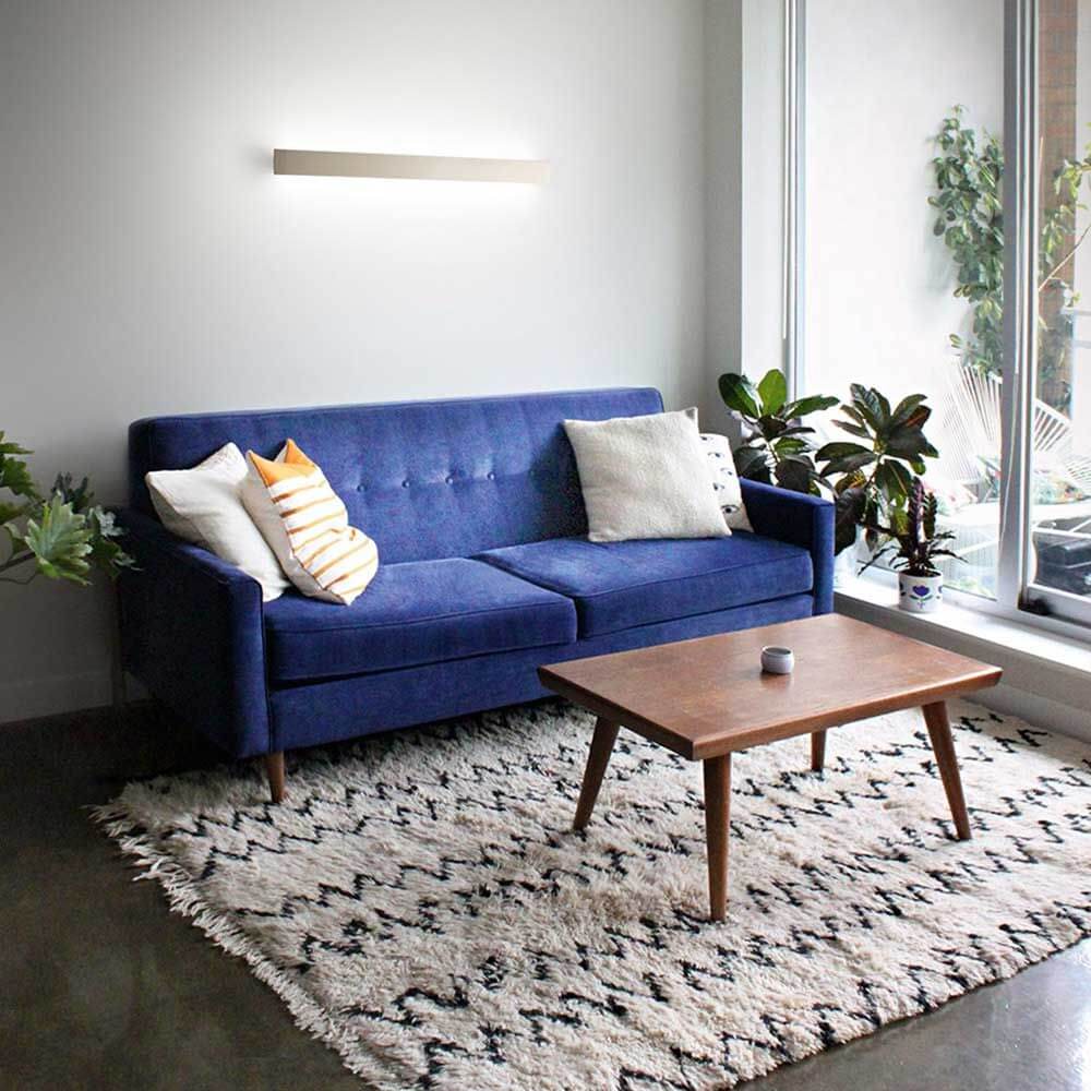 LED Wandleuchte Lotus Aluminium über einem blauen Sofa im modernen Wohnzimmer.
