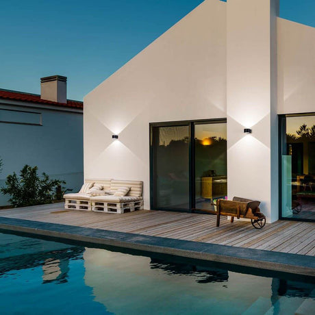 Lao LED Wandlampe IP65 Schwarz an einem modernen Haus mit Pool und Holzterrasse bei Abenddämmerung.