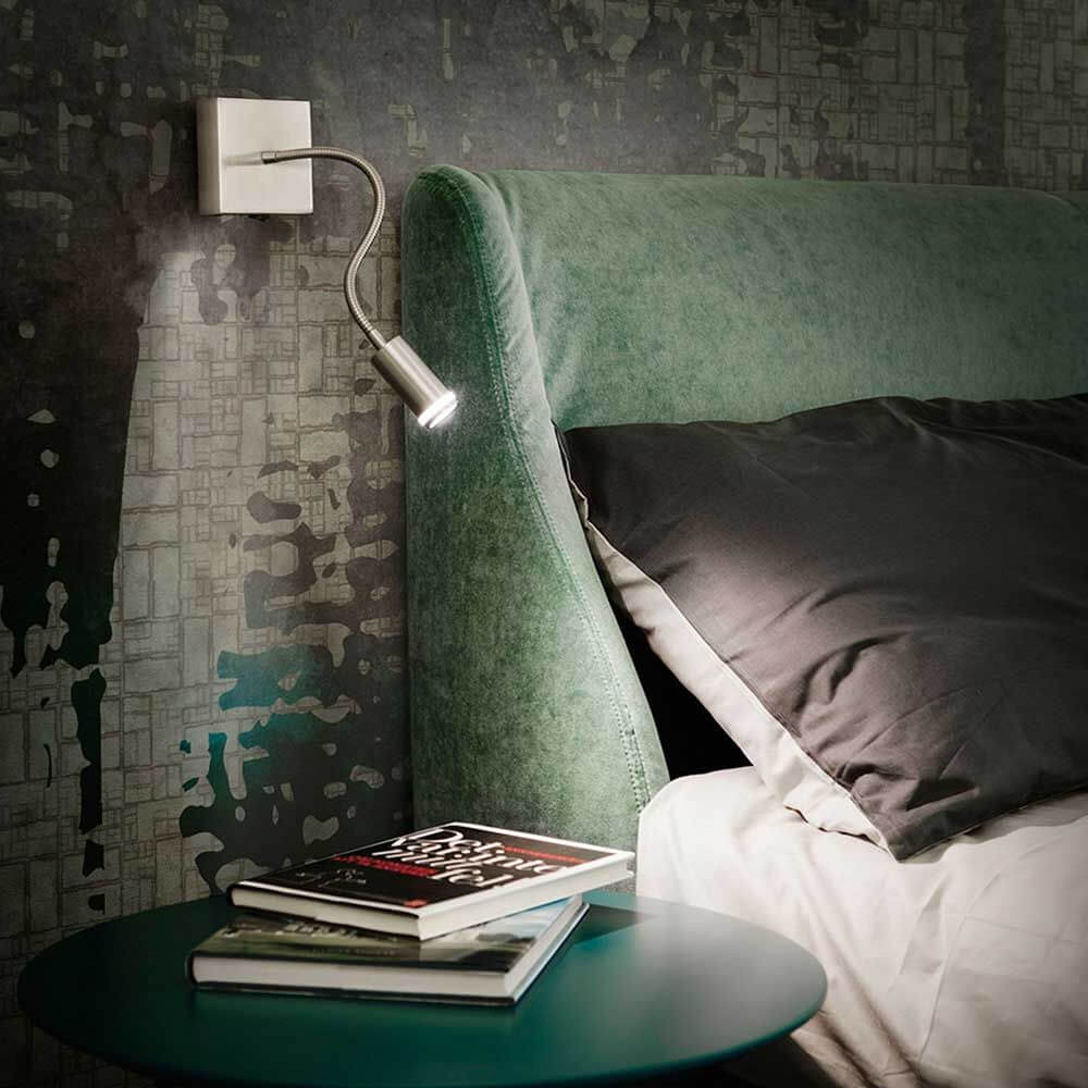 Moderne Portici LED Wandleuchte Nickel neben einem Bett mit grüner Kopfteil und Tisch.