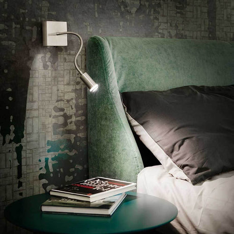 Moderne Portici LED Wandleuchte Nickel neben einem Bett mit grüner Kopfteil und Tisch.