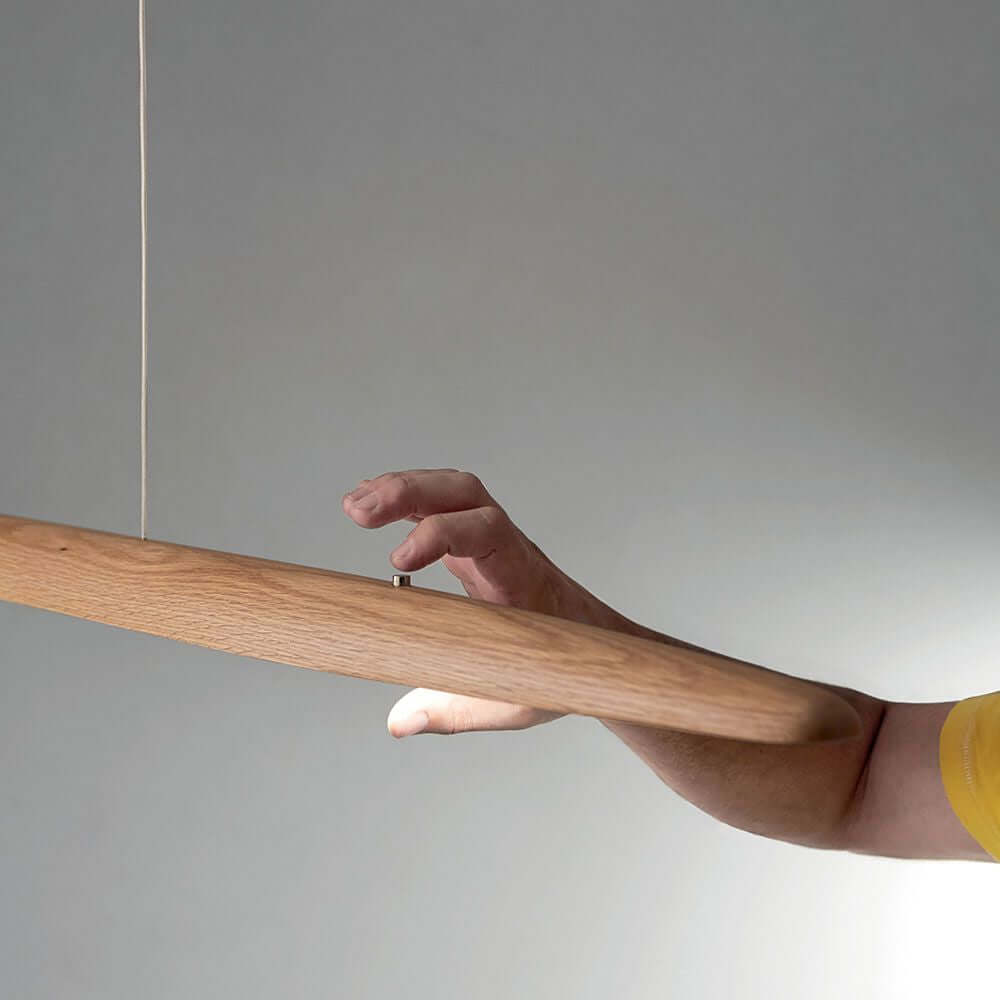 Ribot LED Pendelleuchte 130cm Eichenholz mit Hand, die den integrierten Tastdimmer betätigt.