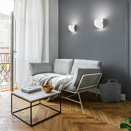Moderne Wohnatmosphäre mit Shield LED Wandleuchte aus Metall über einem hellen Sofa und Couchtisch.