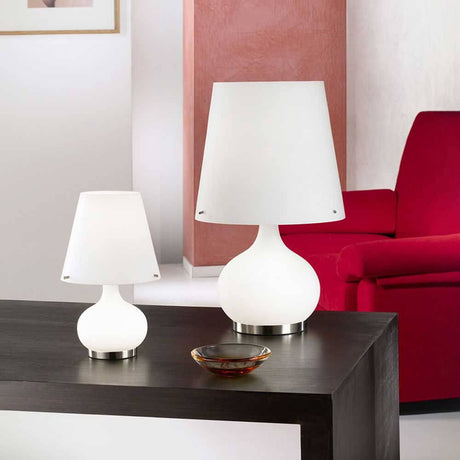 Tischleuchte Ade in Weiß auf einem Tisch, kombiniert mit einem roten Sofa im Hintergrund.