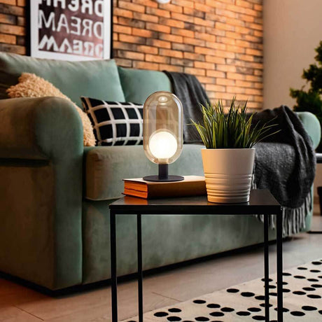 Tischleuchte Gubbio Ø 10cm auf einem Tisch neben einer Pflanze in einem modernen Wohnzimmer.