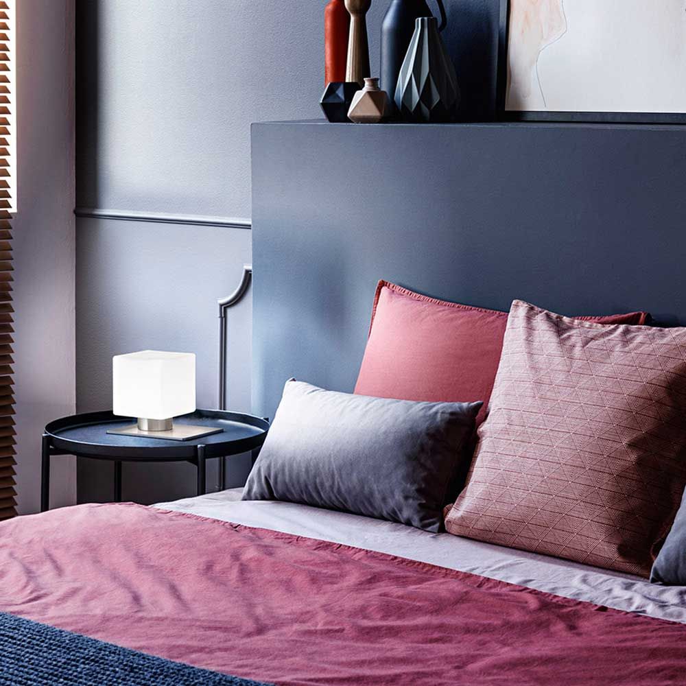 Tischlicht Zara 3000K auf Nachttisch neben Bett mit bunten Kissen in modernem Schlafzimmer-Design.