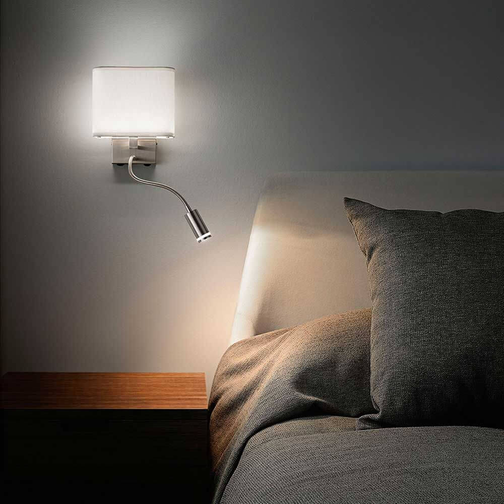 Moderne LED Wandleuchte Vietri neben einem Bett mit Kissen auf einem Nachttisch.