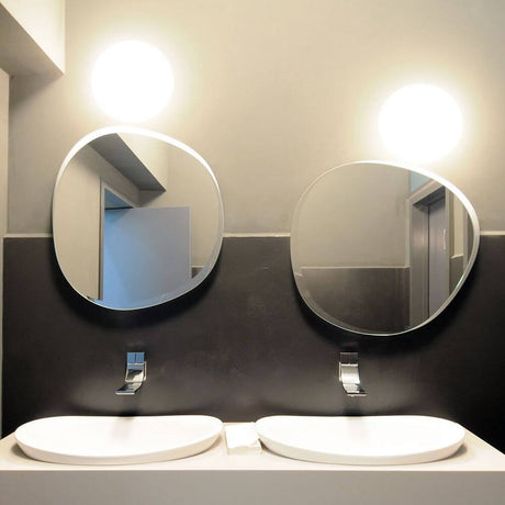 Fabbian Lumi Wandlampe Sfera Ø 20cm über zwei Waschbecken im modernen Badezimmer mit ovalen Spiegeln.