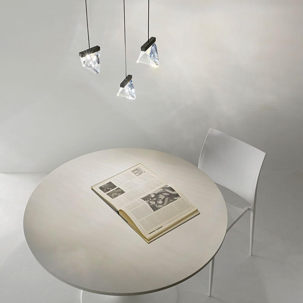 Fabbian Tripla LED-Hängelampe 3-flammig über einem runden Tisch mit einem Buch und einem Stuhl.