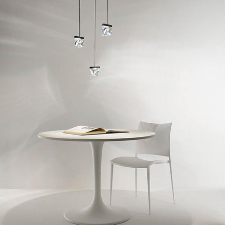 Fabbian Tripla LED-Hängelampe 3-flammig über einem weißen Tisch mit einem Buch und einem Stuhl.