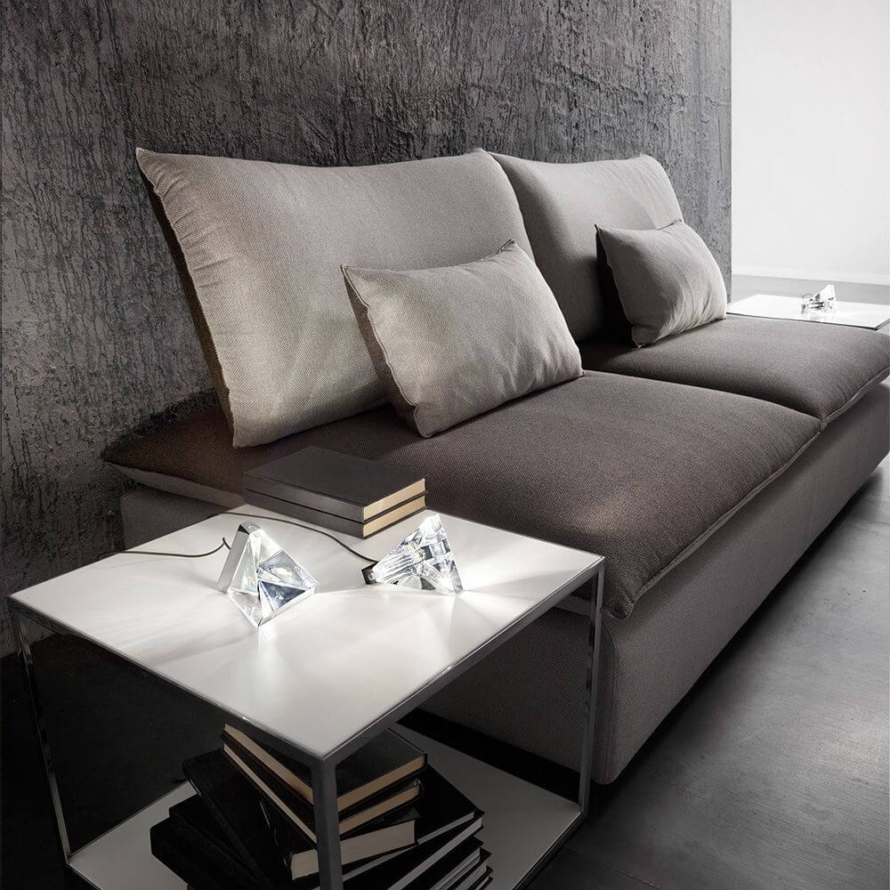 Fabbian Tripla LED-Tischleuchte auf einem modernen Tisch neben einer eleganten Couch mit Kissen.