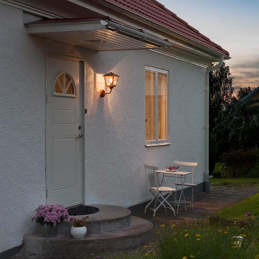 Fenix utendørs vegglampe i akrylglass i kobber ved en inngangsdør i skumringen