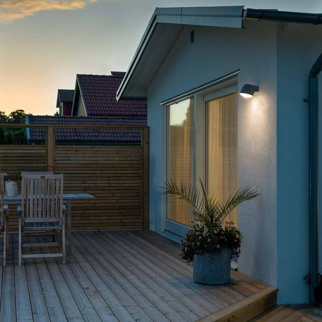 Luz de parede exterior LED Ferrera preta, vidro fosco ilumina um terraço moderno ao pôr do sol.
