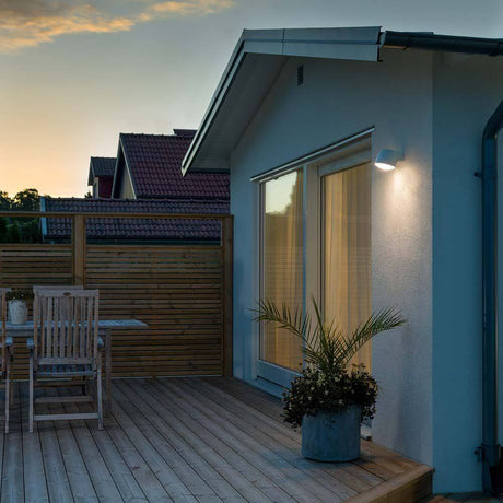 Lampada da parete esterna LED Ferrera bianca, vetro satinato su una parete moderna di una casa su una terrazza al crepuscolo.
