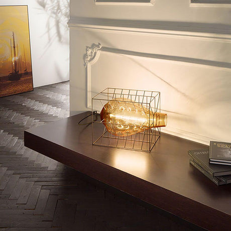 Attimo Tischlampe Muranoglas im Käfig auf einem Tisch, beleuchtet und stilvoll inszeniert.