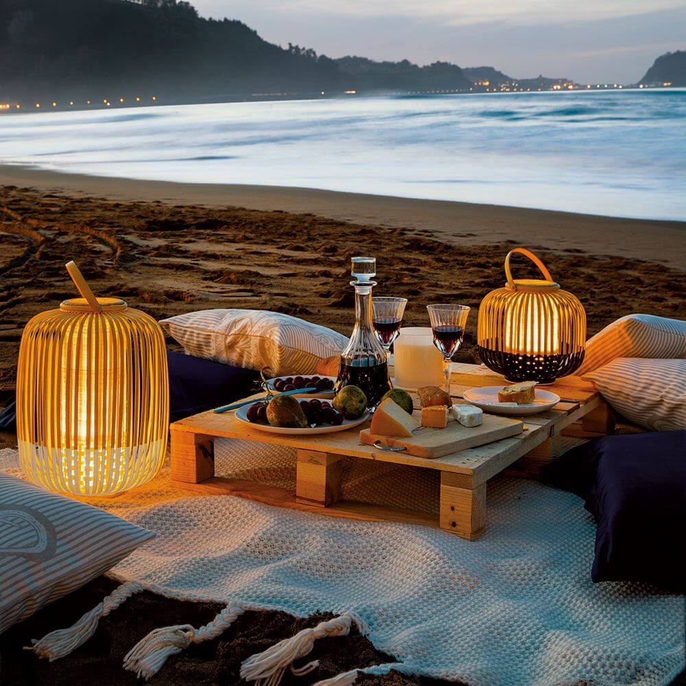 Forestier LED Akku-Bodenleuchte Take A Way IP66 auf einem Strandtisch mit Abenddämmerung und Getränken.