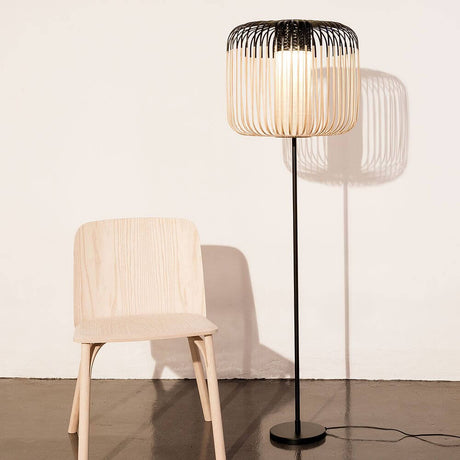 Forestier Stehlampe Bamboo Light 150cm neben einem hellen Holzstuhl auf einem modernen Boden.