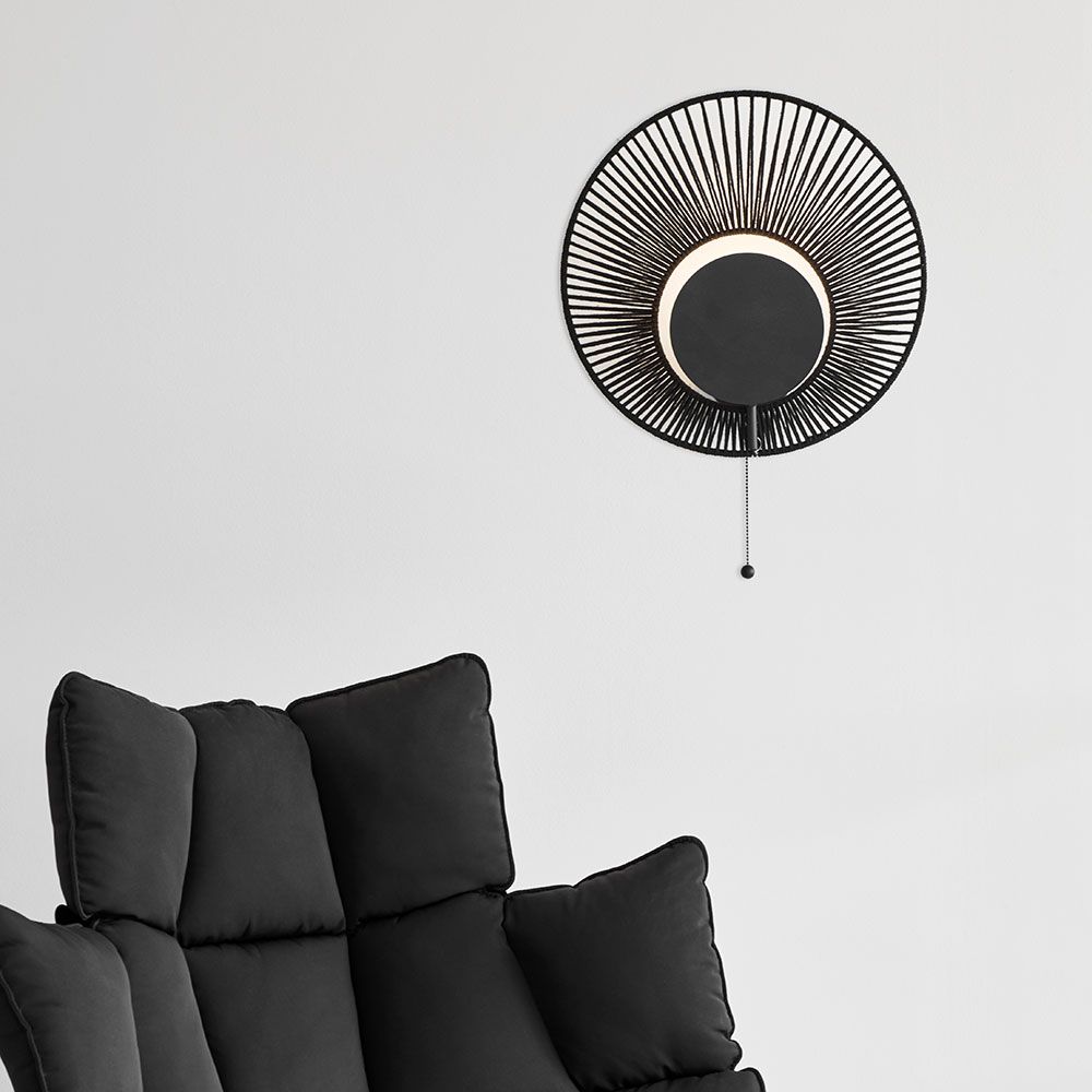 Forestier Wandleuchte Oyster mit Zugkabel an einer Wand über einem bequemen schwarzen Sofa.