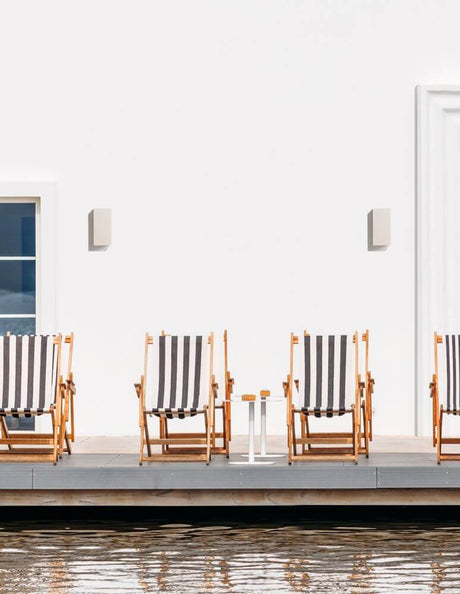 Fuento udendørs væglampe H 18cm beton IP65 next to comfortable lounge chairs at a water table.