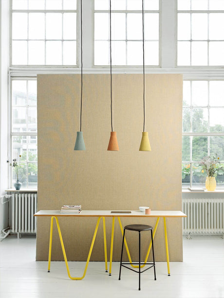Gantlights S1 betongpendelampe med rillet design over en moderne arbeidsplass med gult bord og minimalistisk dekor.