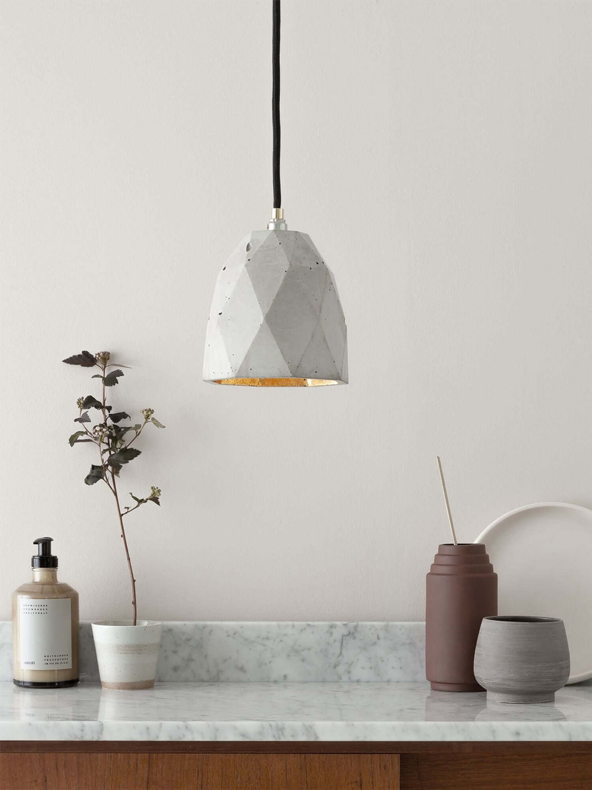 Gantlights T1 Pendelleuchte Beton in minimalistischer Einrichtung auf einem Tisch mit Pflanzen und Dekor.