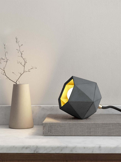 Gantlights T2-Up Tischlampe Beton auf einem Tisch mit geometrischem Design und goldener Innenseite.