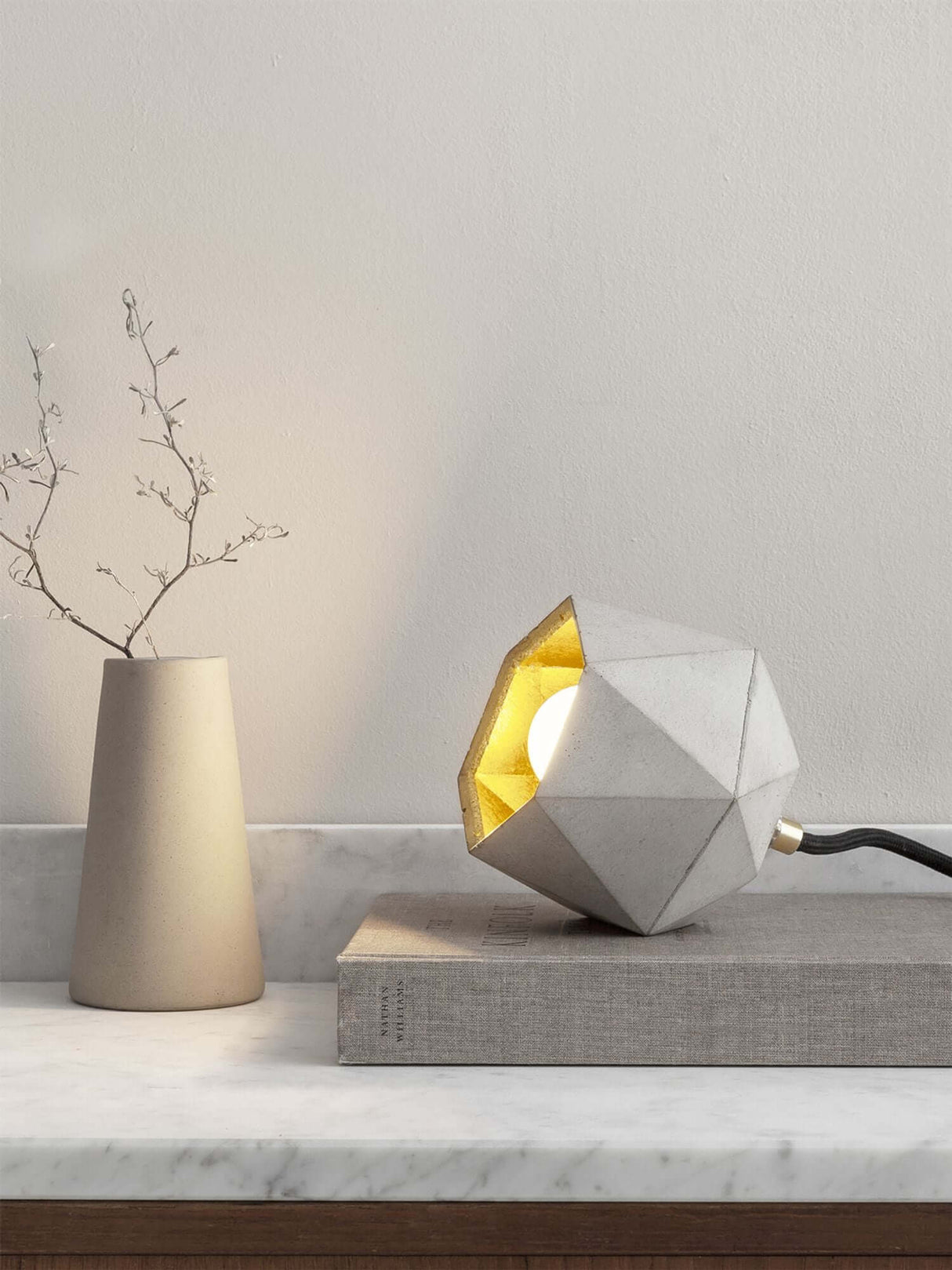 Gantlights T2-Up Tischlampe Beton auf einem Tisch mit geometrischer Form und goldener Innenseite.