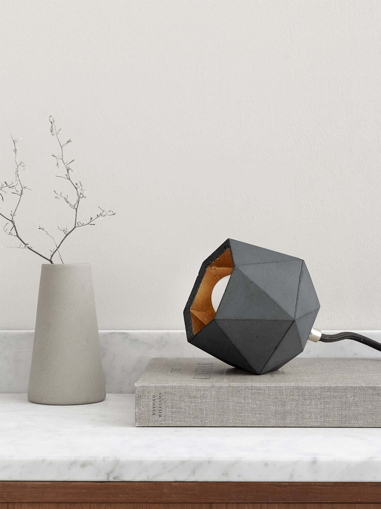 Gantlights T2-Up Tischlampe Beton auf einem Tisch mit geometrischem Design und goldener Innenseite.