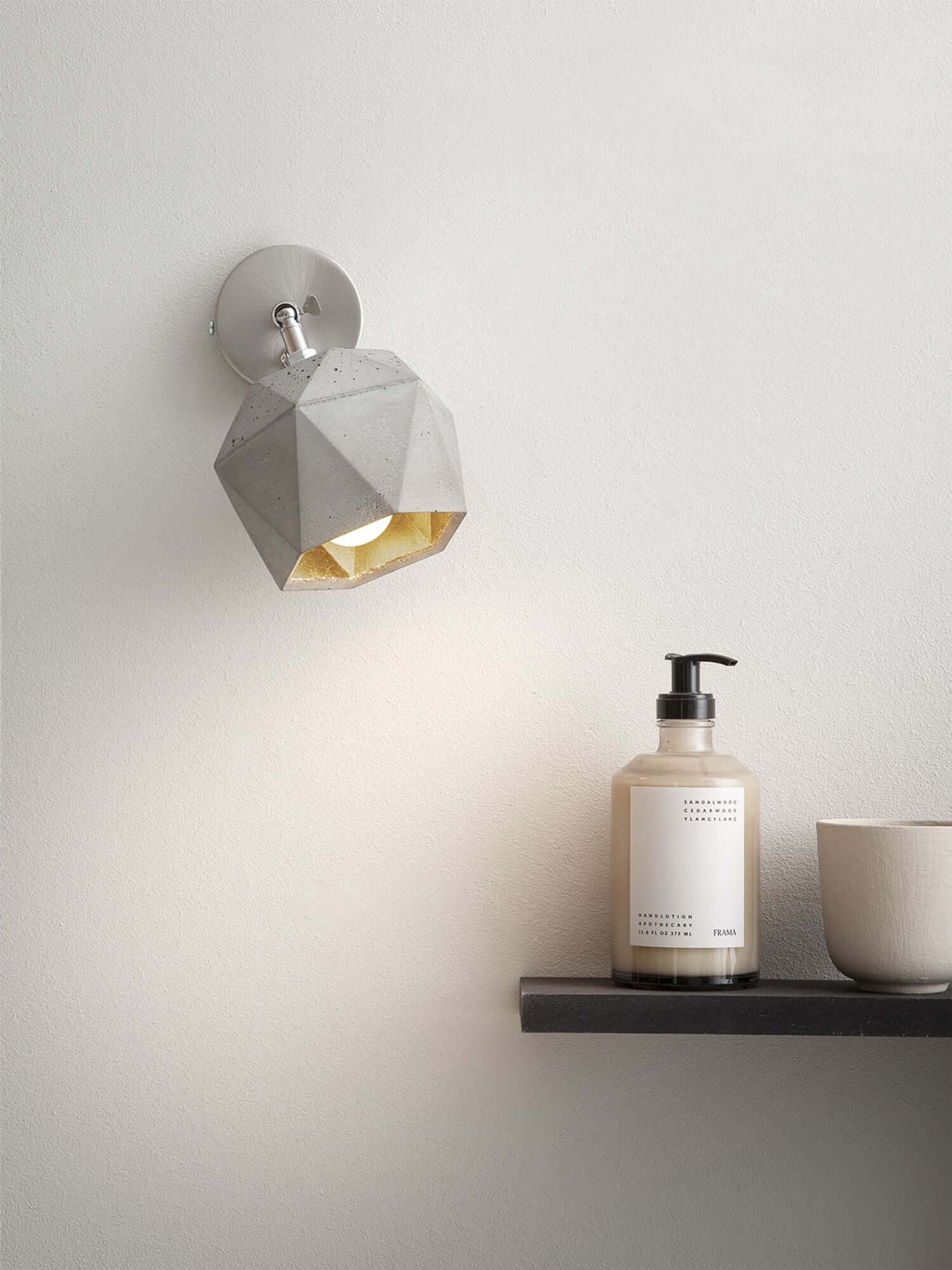 Gantlights T2 Wandspot Beton trianguliert an einer Wand mit Dekorationsobjekten.