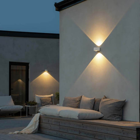 Gela LED Außenwandleuchte Up & Downlight an einer Wand mit warmem Licht und gemütlicher Sitzgelegenheit im Freien.