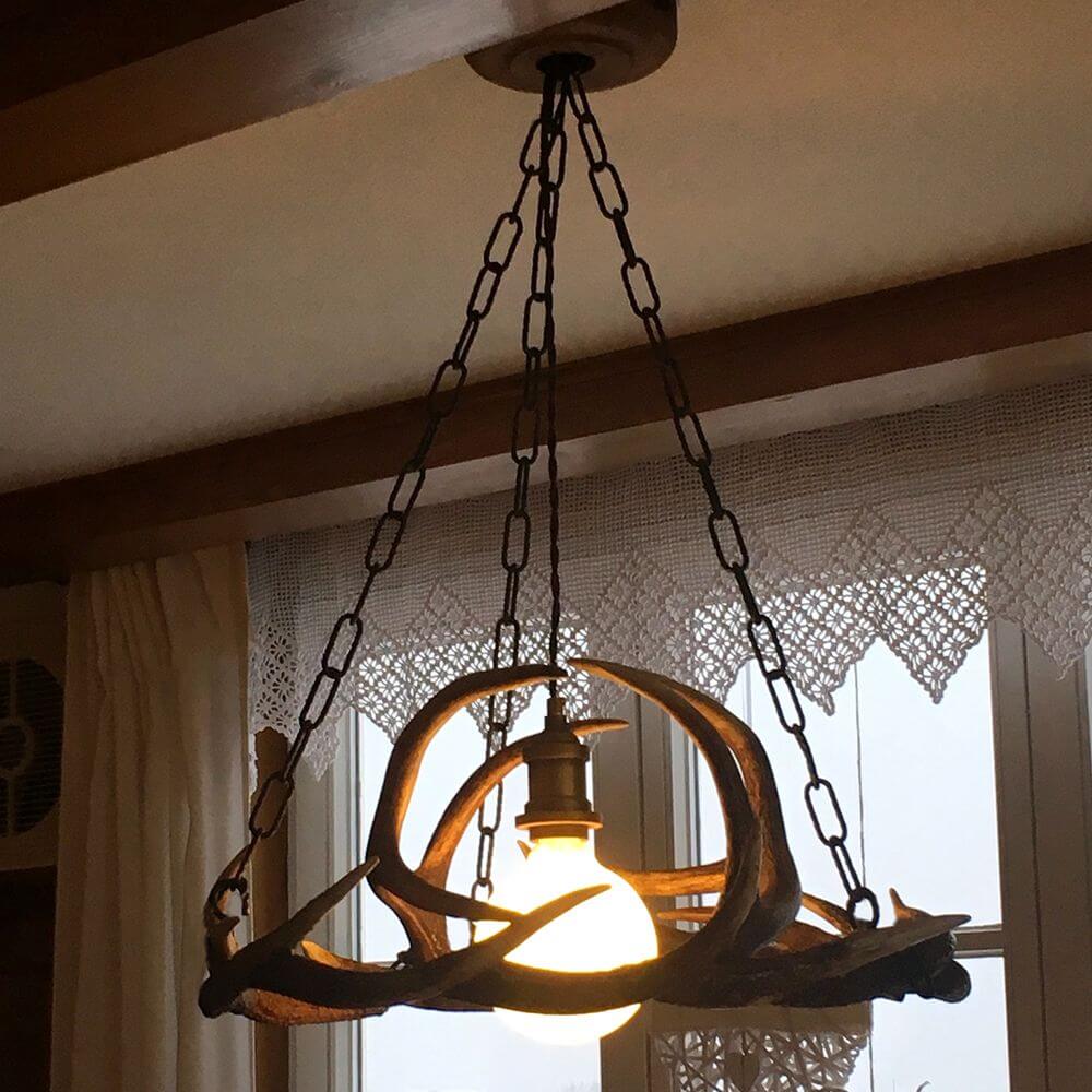 Geweih Chalet Pendellampe Ø 50cm in einem stilvollen Raum mit natürlichem Licht.