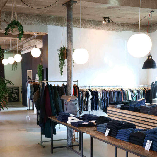 Moderne Boutique mit gemütlicher Atmosphäre, beleuchtet durch runde Lampen und voll mit stilvoller Kleidung.