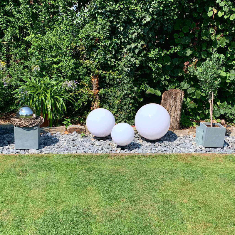 Dekorative weiße Kugeln und Pflanzen in einem modernen Garten mit Steinen und urbanem Flair.