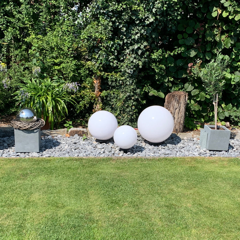 Dekorative weiße Kugeln und Pflanzen in einem modernen Garten mit Steinen und urbanem Flair.