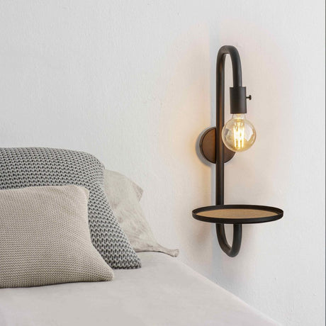 Guest vegglampe med seng med hylle, svart, ved siden av en seng, opplyst med en lyspære.