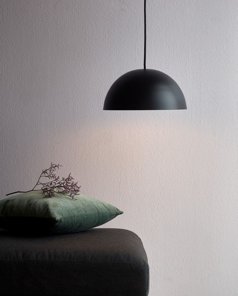Hängelampe Ellen 30 Schwarz über einem Tisch mit grauer Decke und grünen Kissen, minimalistisch und skandinavisch.