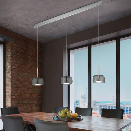 LED Suspension Flute Chrome au-dessus d’une table à manger avec des verres rapportés transparents et gris fumé.