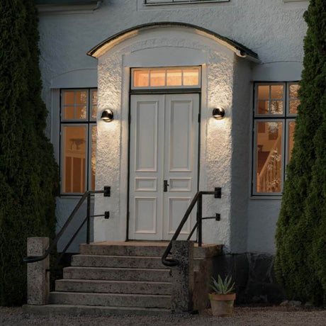 Hild 2-pære udendørs væglampe installeret ved siden af hoveddøren til et hus, stærkt oplyst og elegant.