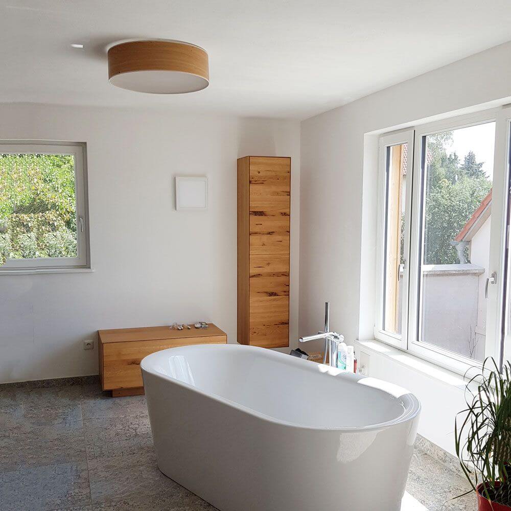 Holz-Deckenleuchte Discus Deutsche Eiche über eleganter Badewanne in modernem Badezimmer.