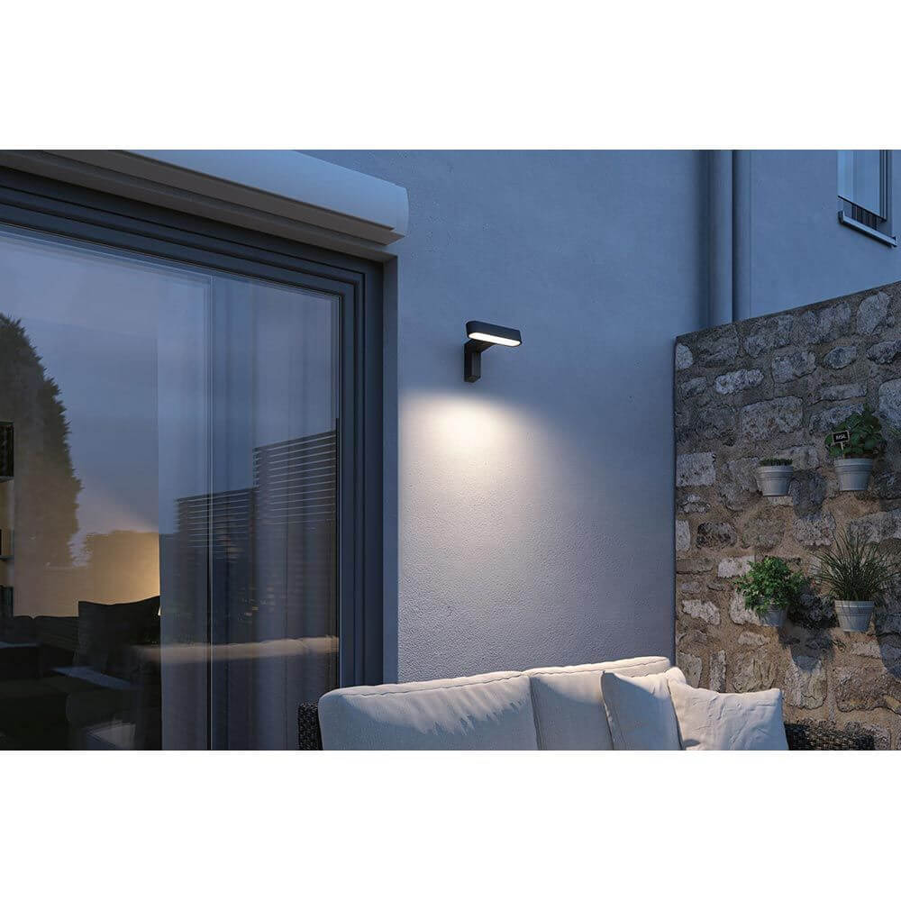 House LED Außenwandleuchte Ito mit Bewegungssensor an einer Hauswand mit gemütlicher Sitzgelegenheit im Freien.