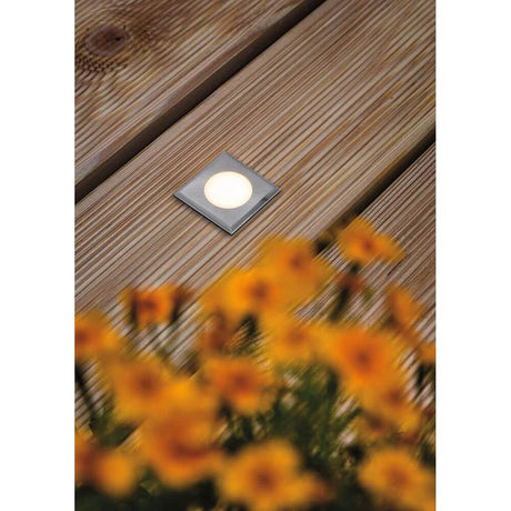 House LED square stainless steel floor recessed light IP67 on a wooden deck with blooming flowers in the foreground.