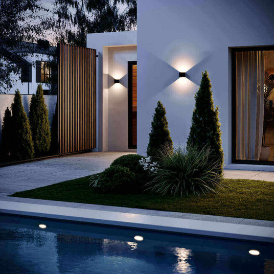 Elegante Außenbeleuchtung am modernen Haus mit Hecken, Rasen und Pool im nächtlichen Ambiente.